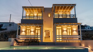 Una casa moderna de dos pisos con piscina, mobiliario exterior y una escalera que conduce al nivel superior.