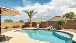 A swimming pool with a curved edge, surrounded by a brick wall, palm trees, and a clear blue sky. - Golf, Gamble, Relax Poolside! Maricopa Desert Home (Maricopa)