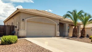 A single-story house with a large garage, a small front yard with a palm tree, and a clear blue sky. - Golf, Gamble, Relax Poolside! Maricopa Desert Home (Maricopa)