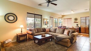 A living room with a sectional sofa, a coffee table, a floor lamp, and a ceiling fan. - Golf, Gamble, Relax Poolside! Maricopa Desert Home (Maricopa)