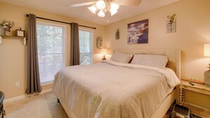 Een slaapkamer met een bed, een plafondventilator, een raam met gordijnen, een nachtkastje met een lamp en een wandklok.