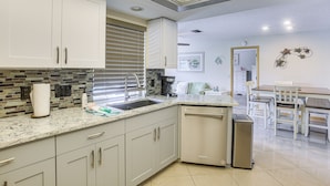Een moderne keuken met witte kastjes, een granieten aanrechtblad, een vaatwasser en een eethoek met een tafel en stoelen.