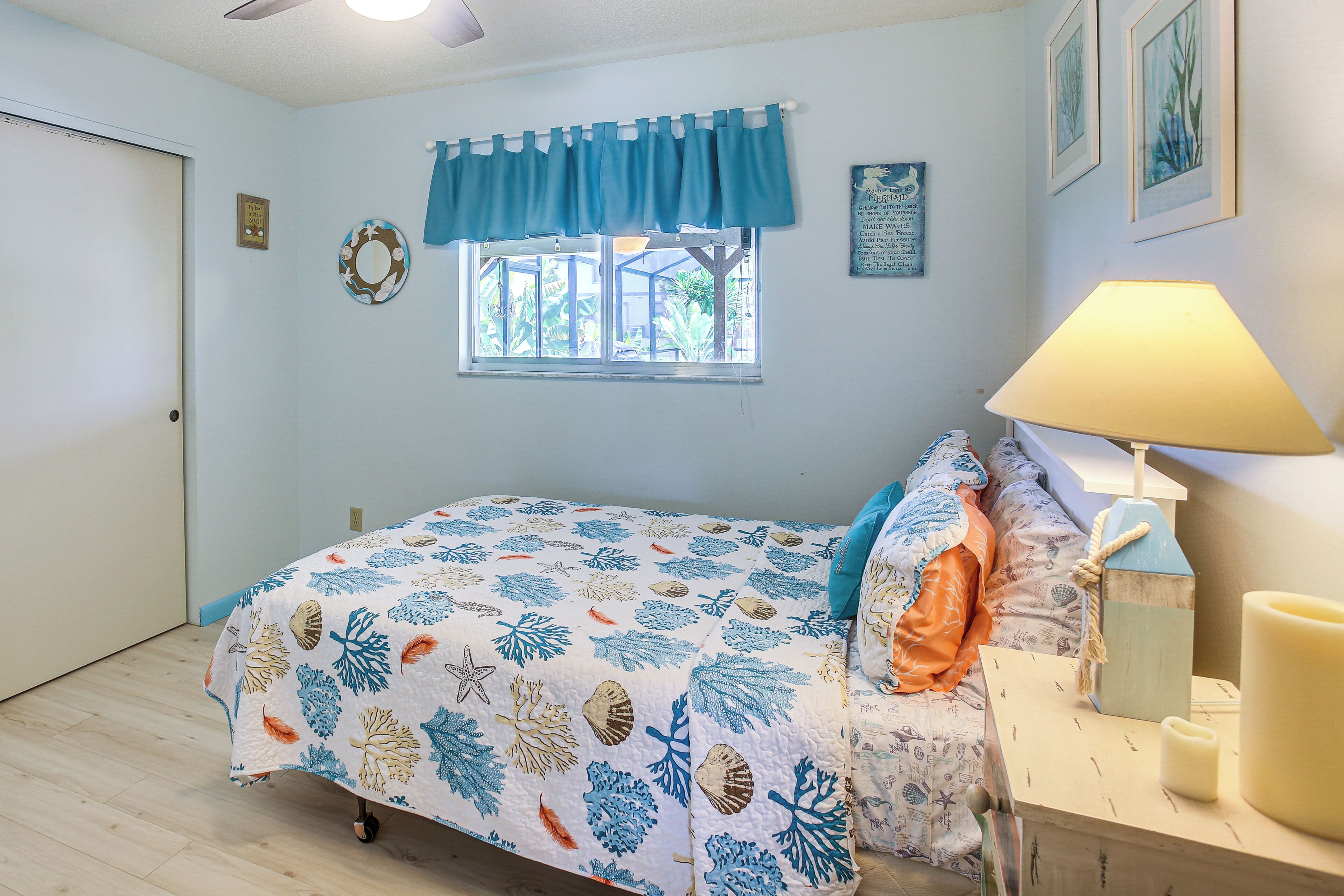Un dormitorio con cama, ventana con vistas, lámpara y un cuadro en la pared.