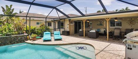 Area piscina con patio coperto, poltrona relax e barbecue.