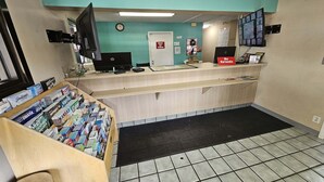 Zona de recepción con mostrador, computadora, televisor, reloj y puerta con letrero.