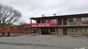 Un Travel Inn con un letrero rojo, un estacionamiento y un área cercada.