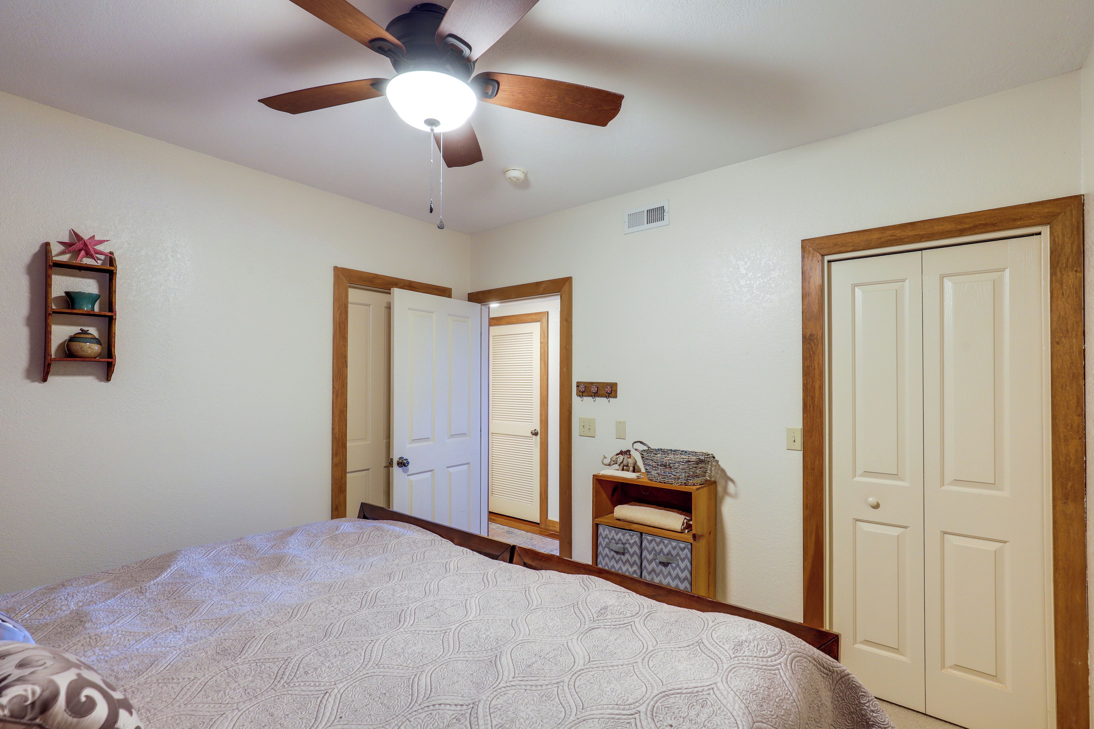 A bedroom with a bed, a ceiling fan, a door, a small shelf, and a closet.