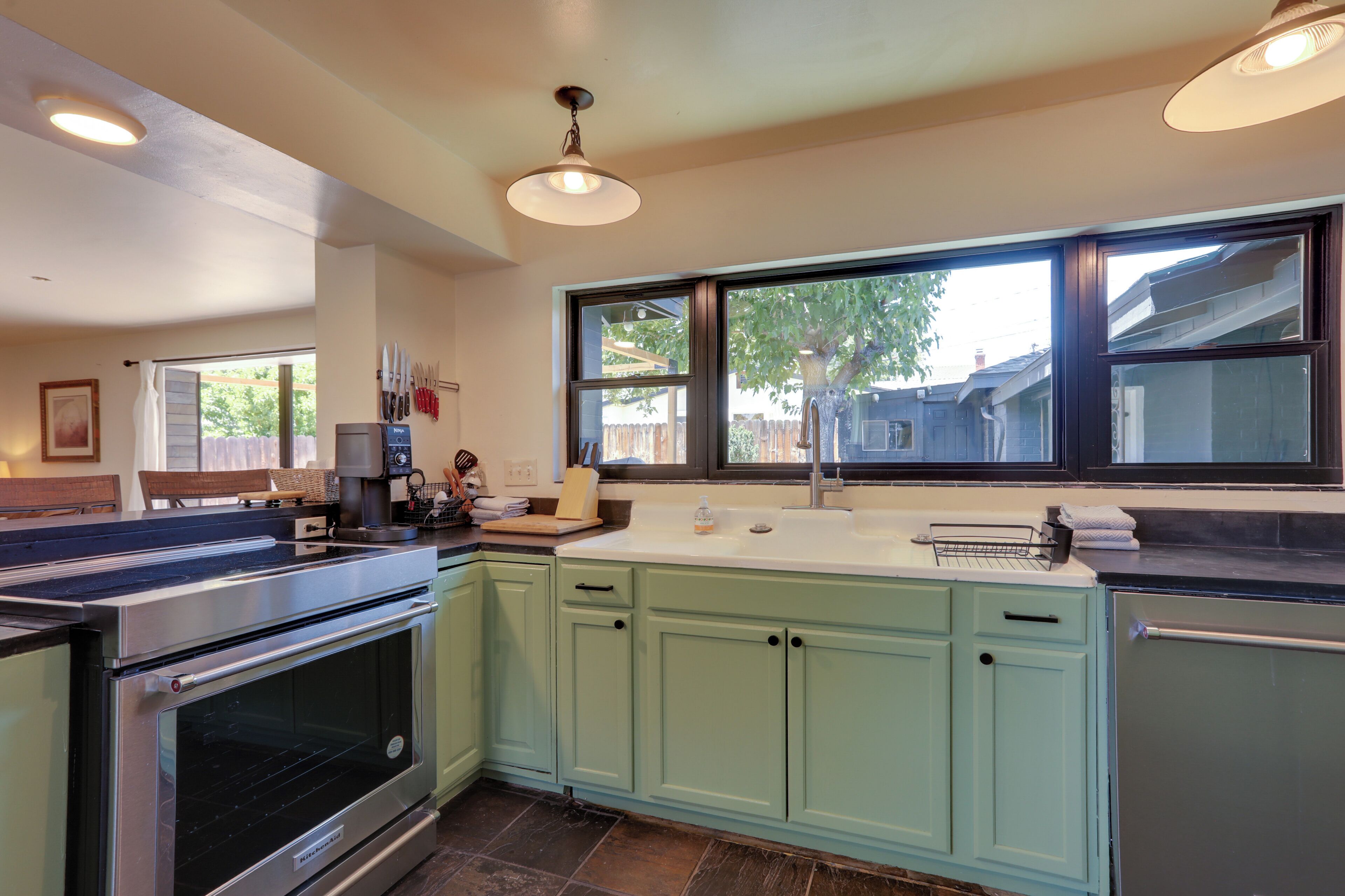 A kitchen with a large window, stainless steel appliances, and light green cabinets.