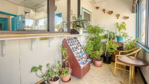 Varanda com plantas em vasos, uma mesa de madeira e um porta-revistas.