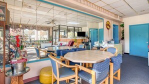 Quarto de hotel com uma janela grande, área de jantar com cadeiras estofadas em azul, uma mesa redonda e uma cozinha compacta.