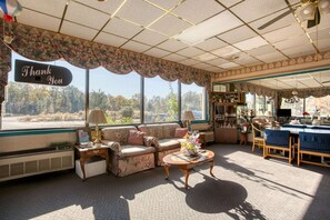 A room with a sofa, a coffee table, a dining table with chairs, a window with a 'Thank You' sign, and a view of trees. - 2 Full Beds|Non-Smoking (Petersburg VA)