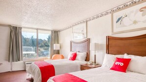 Quarto de hotel com duas camas, janela com vista para carros estacionados, cabeceira de madeira e um quadro na parede.