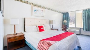 Une chambre d’hôtel avec un grand lit, deux tables de chevet, une commode, une fenêtre avec des rideaux et un tableau accroché au mur.