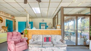 A lobby with a pink armchair, floral sofa, and a reception desk with a clock on the wall. - 2 Full Bed|Smoking|Petersburg VA (Petersburg VA)