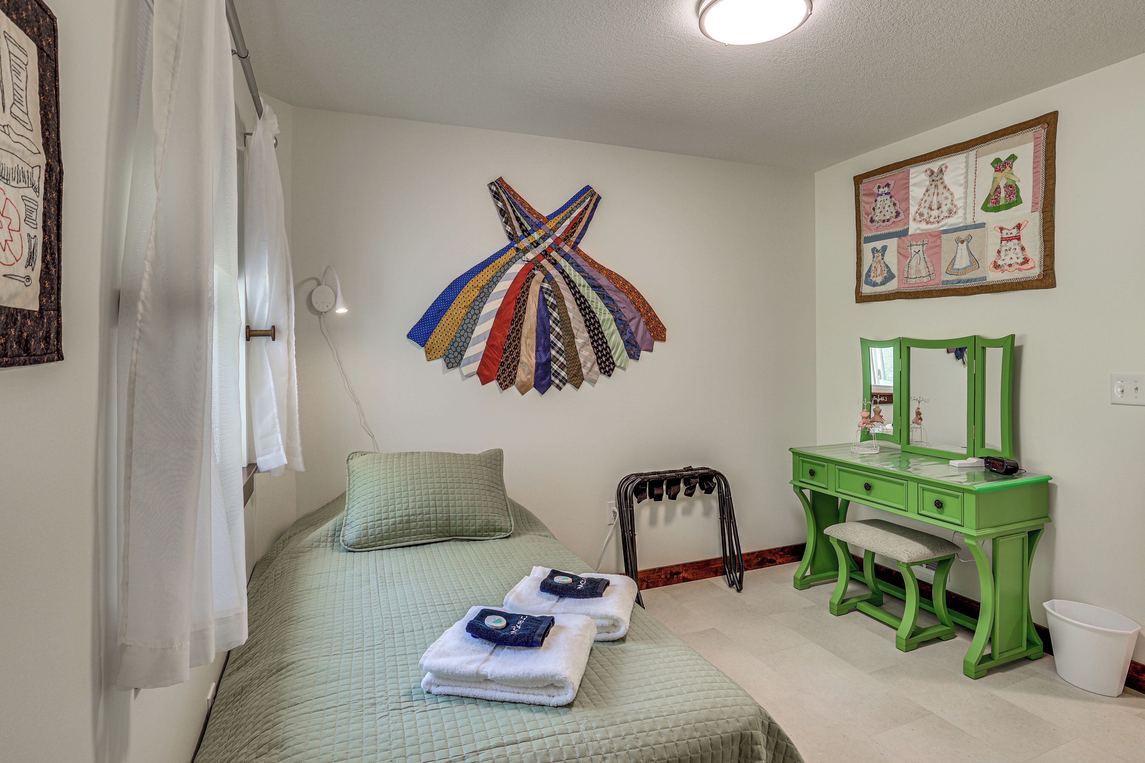 A bedroom with a bed, a green vanity with a mirror, and a wall art piece.