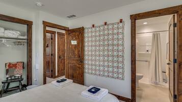 A hotel room with a bed, a wooden wardrobe, a bathroom with a shower, and a patterned wall hanging.