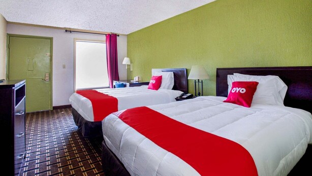 A hotel room with two beds, a desk, a chair, a lamp, a phone, and a window with curtains. - Pensacola FL | 2 Full Bed (Pensacola FL)