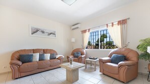 A living room with a sofa, armchairs, a coffee table, and a window with curtains.