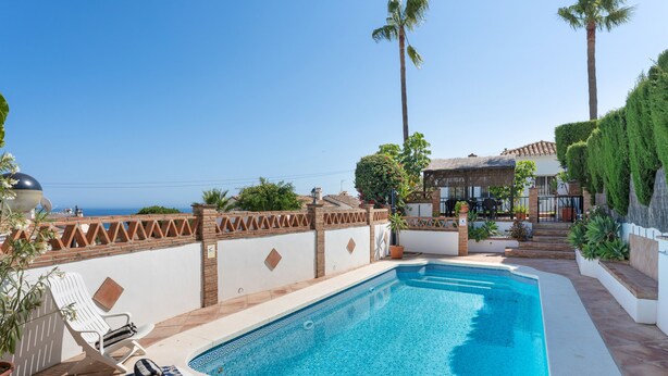 A swimming pool with a tiled edge, lounge chairs, and a view of the sea.