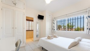 A bedroom with a bed, a TV, a window with bars, and a view of the outside.