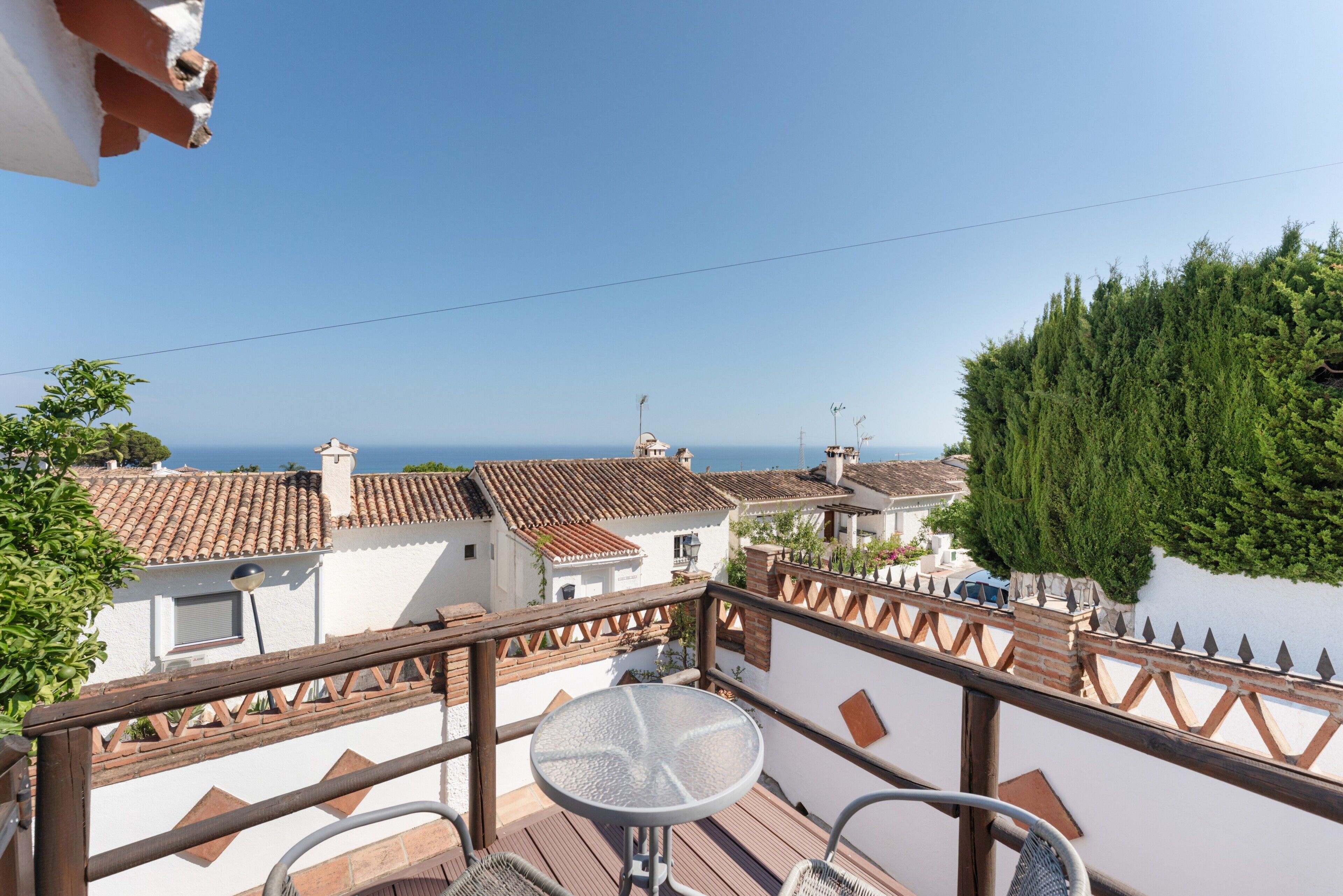 A balcony with a table and chairs, overlooking a coastal area with buildings and a clear sky.