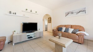 A modern living room with a flat-screen TV, a beige sofa, a coffee table, and a minimalist design.