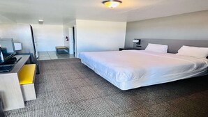 Una camera d'albergo con un letto, una scrivania, una sedia e un comodino con una lampada.