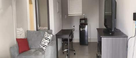 A compact living space with a grey sofa, a small table, a television, and a microwave.