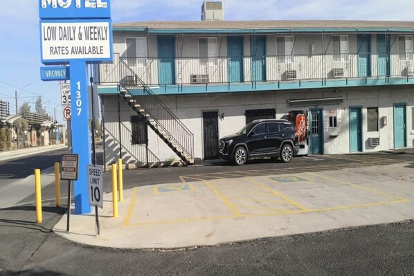 Ett motell med en blå skylt som visar låga dags- och veckopriser, en hastighetsbegränsningsskylt som visar 10, och en parkeringsplats med markerade parkeringsrutor.