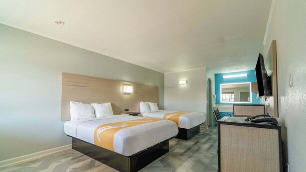 Quarto de hotel com duas camas, uma escrivaninha, televisão e um banheiro ao fundo.