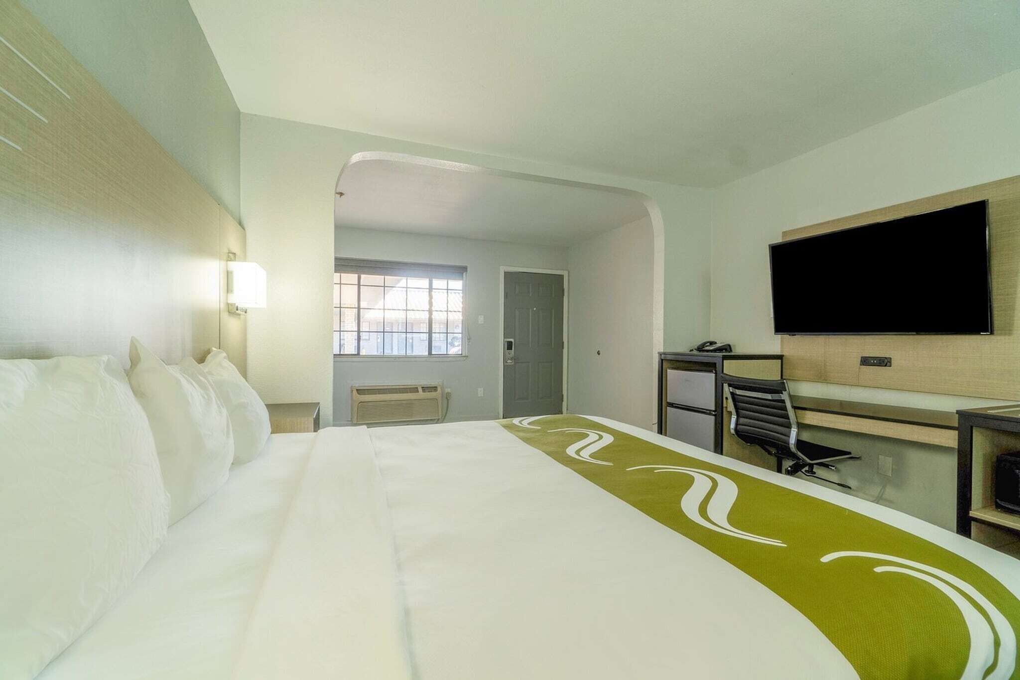 Une chambre d’hôtel avec un lit, un bureau, une chaise, une télévision et une fenêtre.