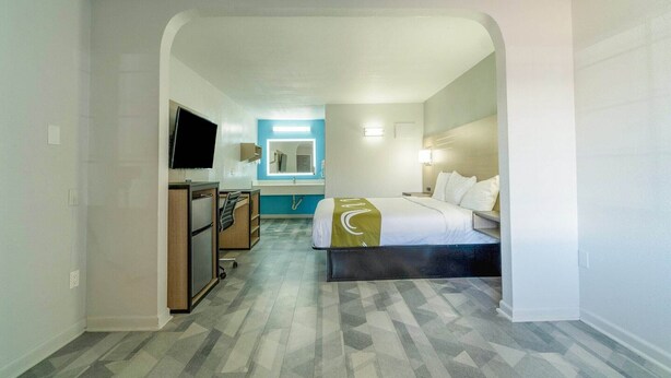 A hotel room with a bed, a desk, a TV, and a bathroom visible through an archway.