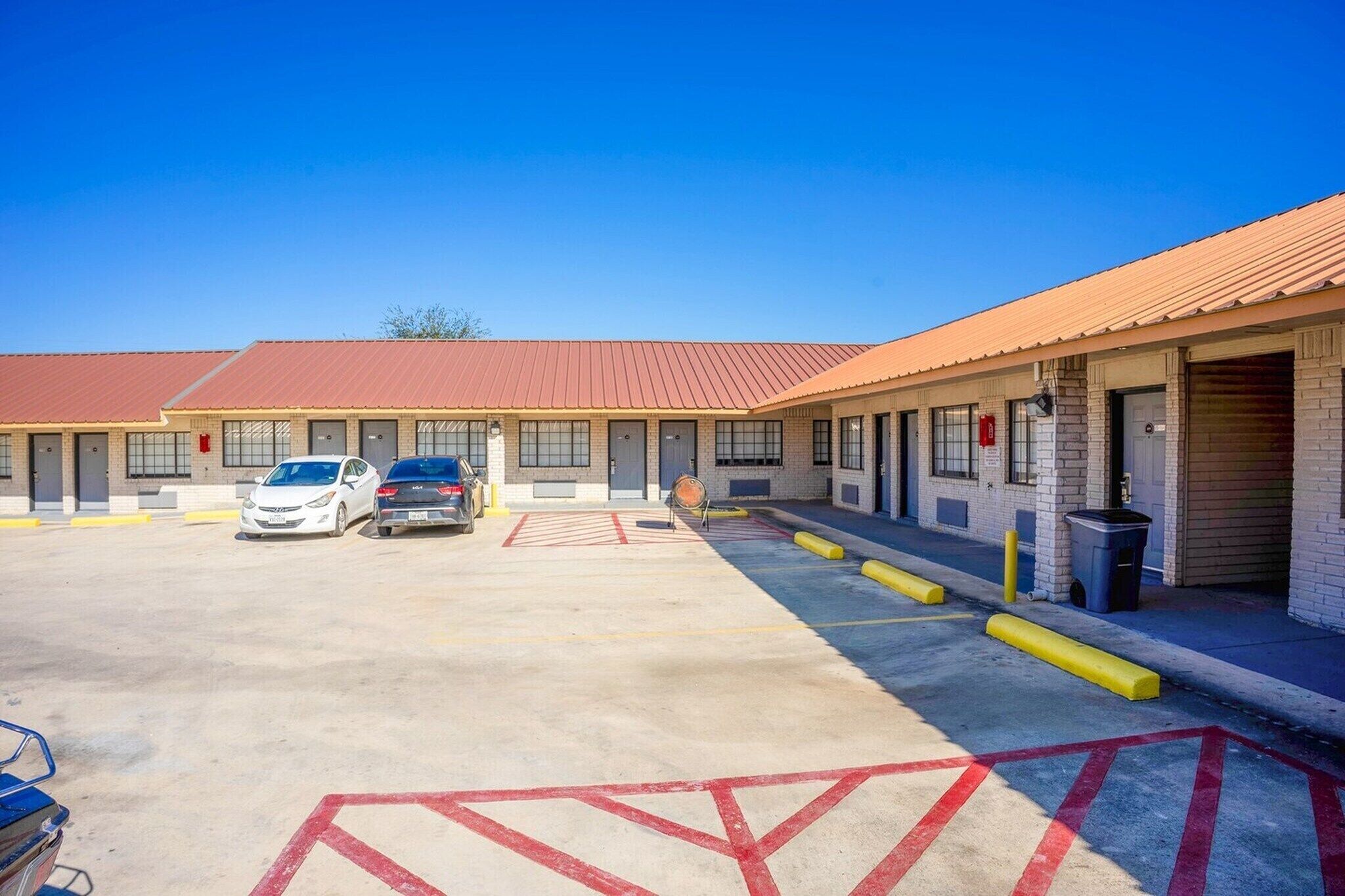 A motel with a parking lot, two cars parked, and a building with a red roof.