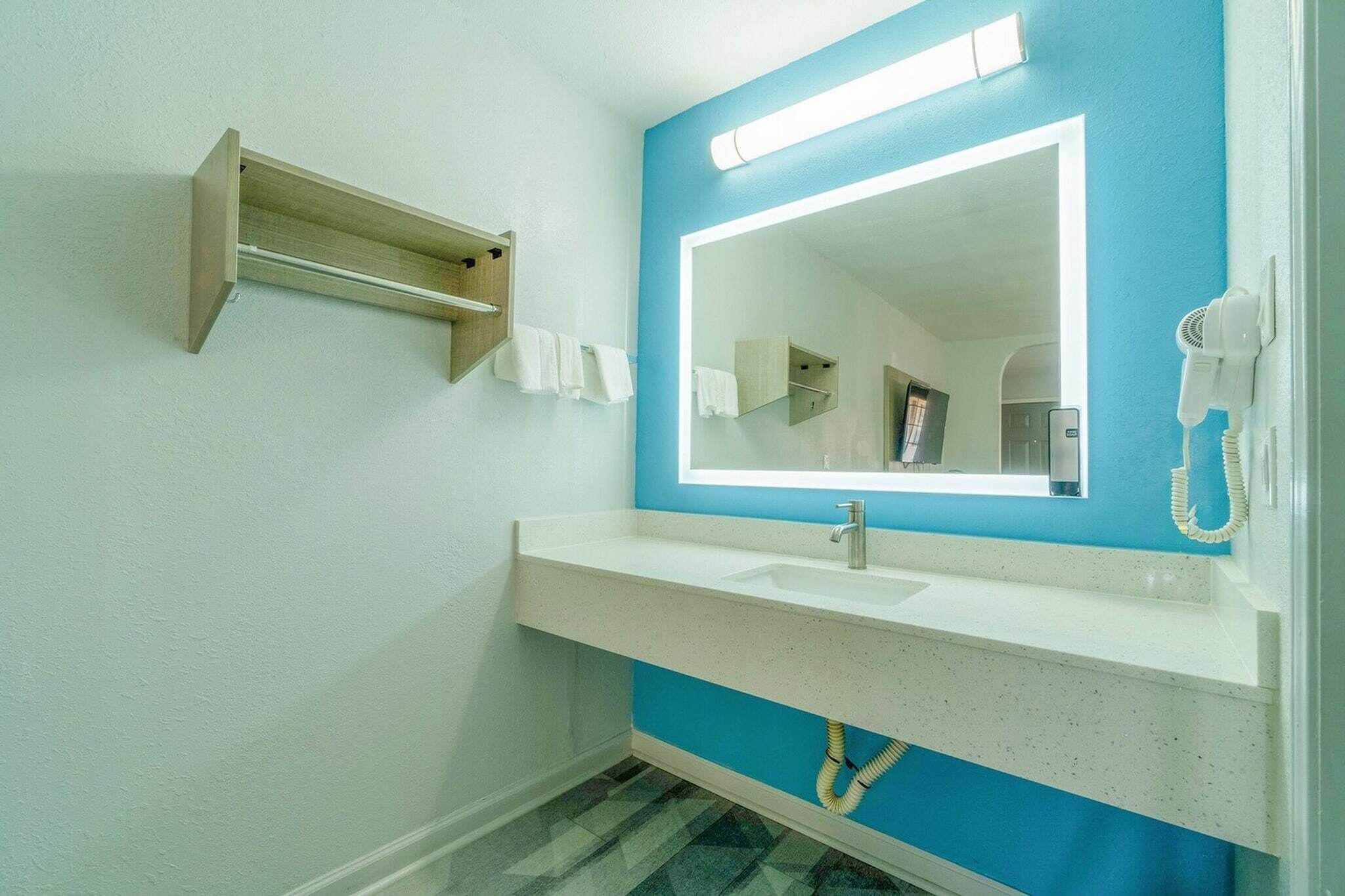 Een badkamer met een wit wastafelmeubel, een blauwe accentmuur, een spiegel, een handdoekhouder en een haardroger.