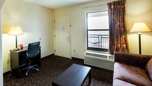 Ett hotellrum med ett skrivbord, en stol, en soffa och ett fönster med gardiner.