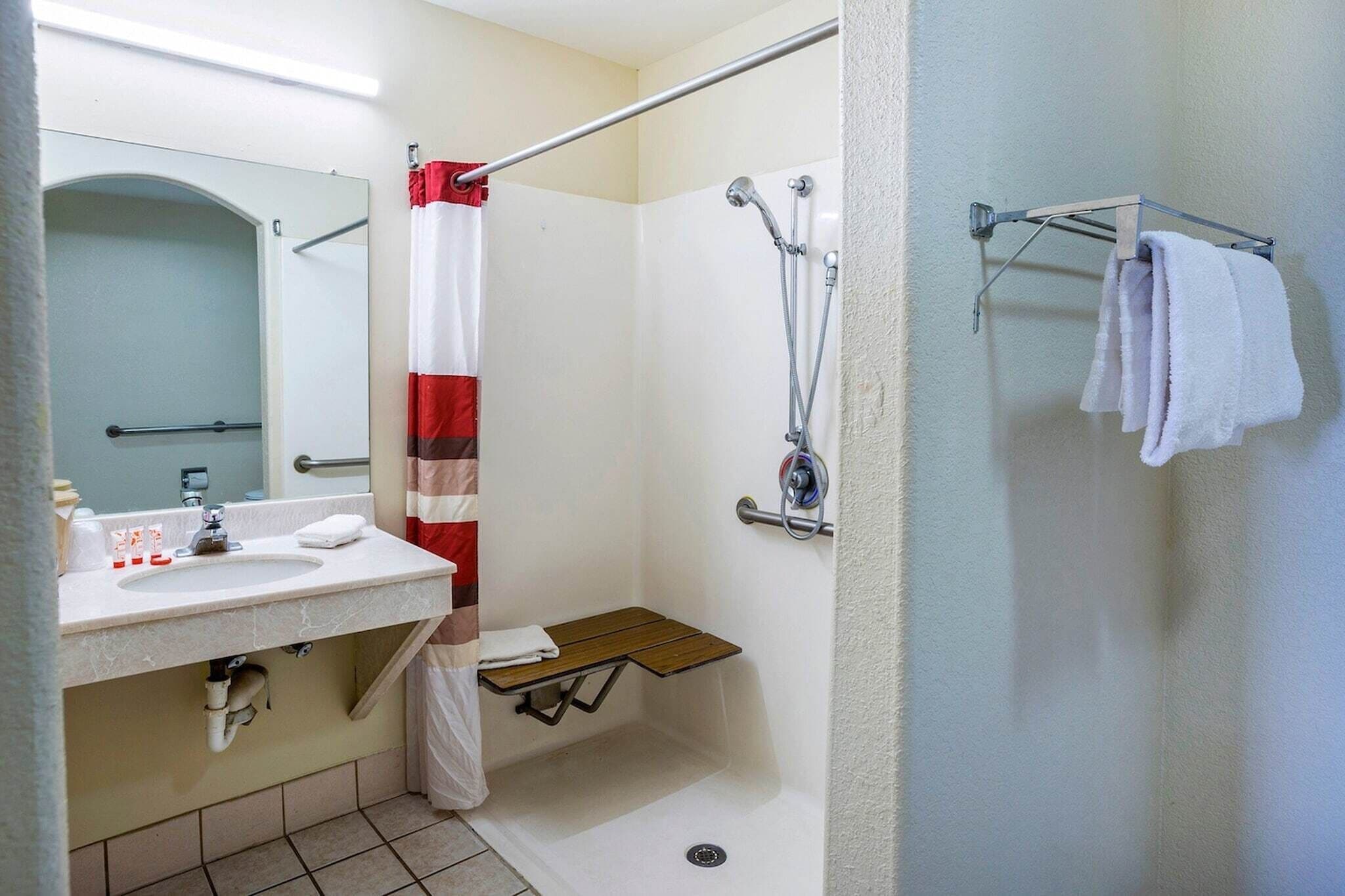 A bathroom with a shower, a sink with toiletries, a towel rack, and a mirror.