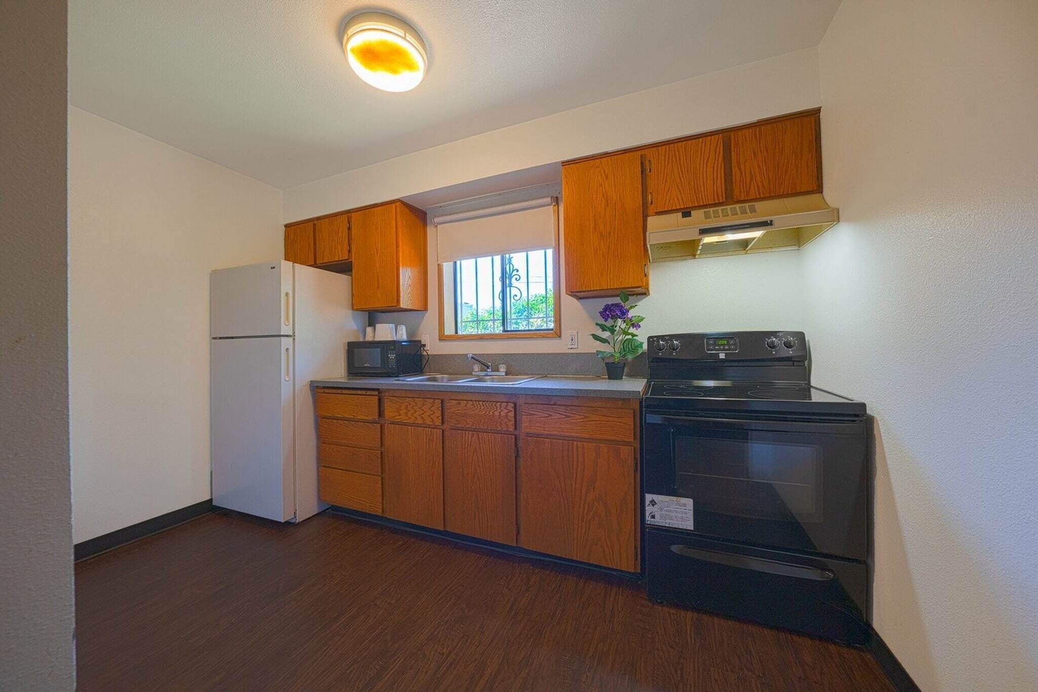 A kitchen with wooden cabinets, a refrigerator, a microwave, a stove, and a window.
