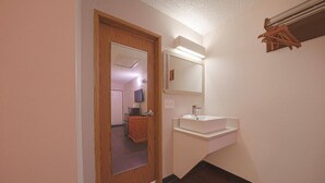 Un couloir avec une porte en bois, un miroir, un lavabo blanc et une étagère en bois.