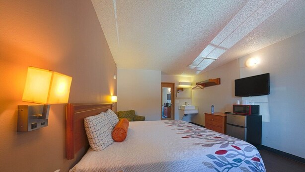 Une chambre d’hôtel équipée d’un lit, d’une lampe de chevet, d’un téléviseur à écran plat, d’un four à micro-ondes et d’un petit bureau avec un téléphone.