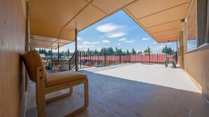 Un espace extérieur abrité avec une chaise en bois, une vue sur un parking clôturé et un bâtiment en arrière-plan.