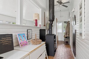 A room with a fireplace, a ceiling fan, a window with a view, and a shelf with books and a basket. - Holiday Close to Forest, Fjord and Beach (Kulhuse)