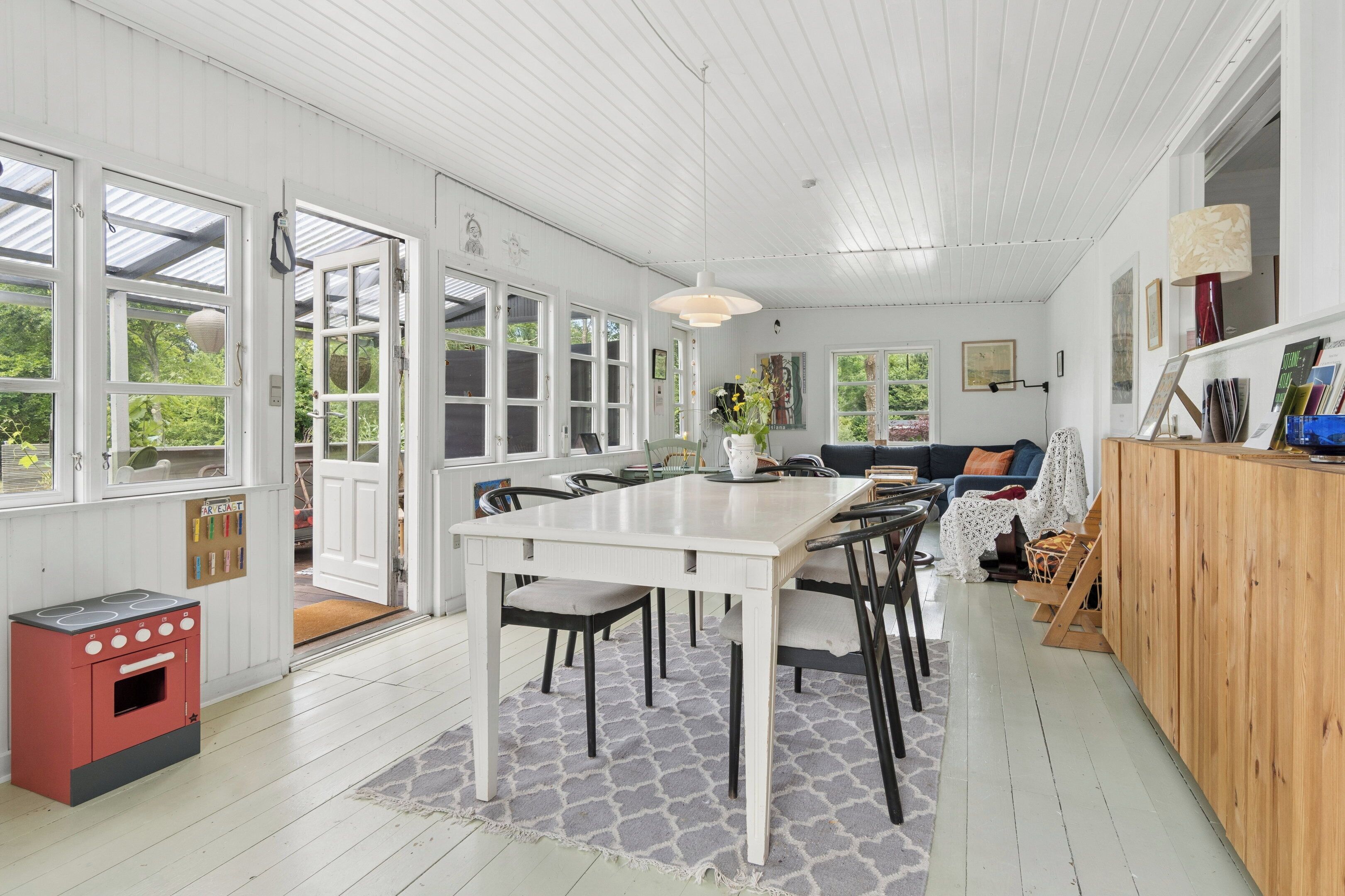 A spacious kitchen with a dining table, chairs, a red stove, and a wooden cabinet.