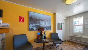 Une chambre d’hôtel avec deux chaises, une table, un grand tableau représentant un paysage urbain, un panneau indiquant « Merci de respecter les lieux » et un panneau indiquant « Dépôt du courrier ».
