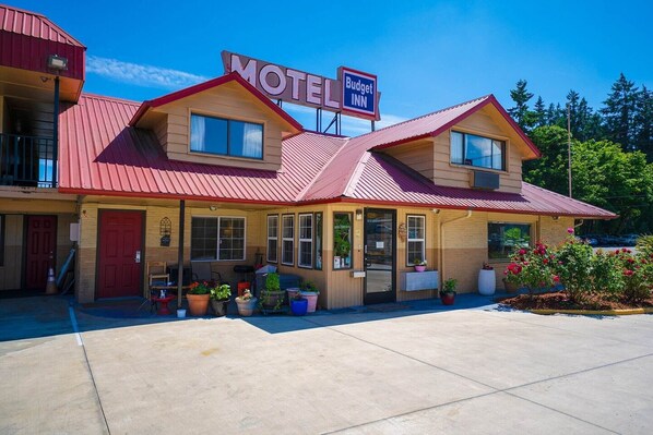 Un motel avec un toit rouge, une enseigne et des plantes en pot devant l’entrée.