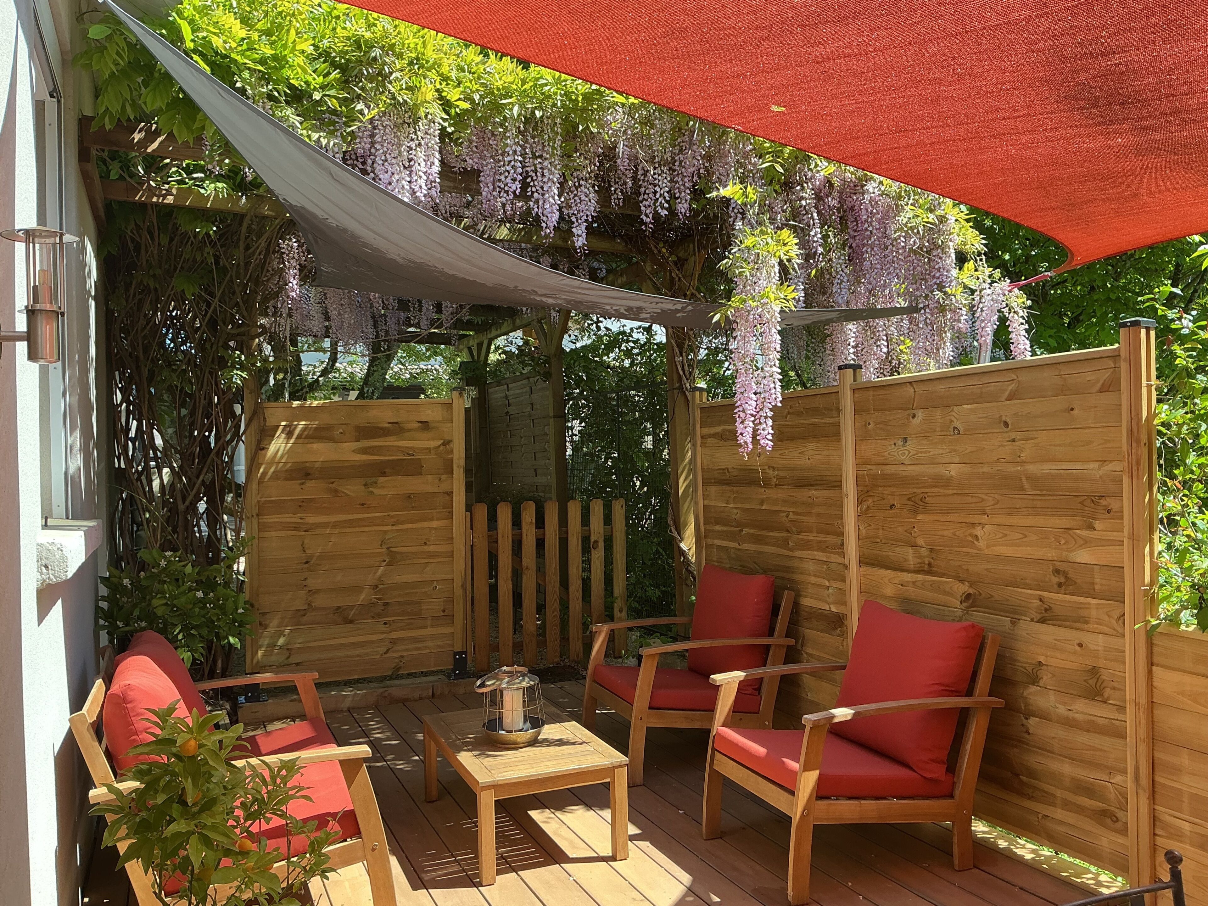 Ett trädäck med utemöbler, en pergola med hängande wisteria och ett trästaket.