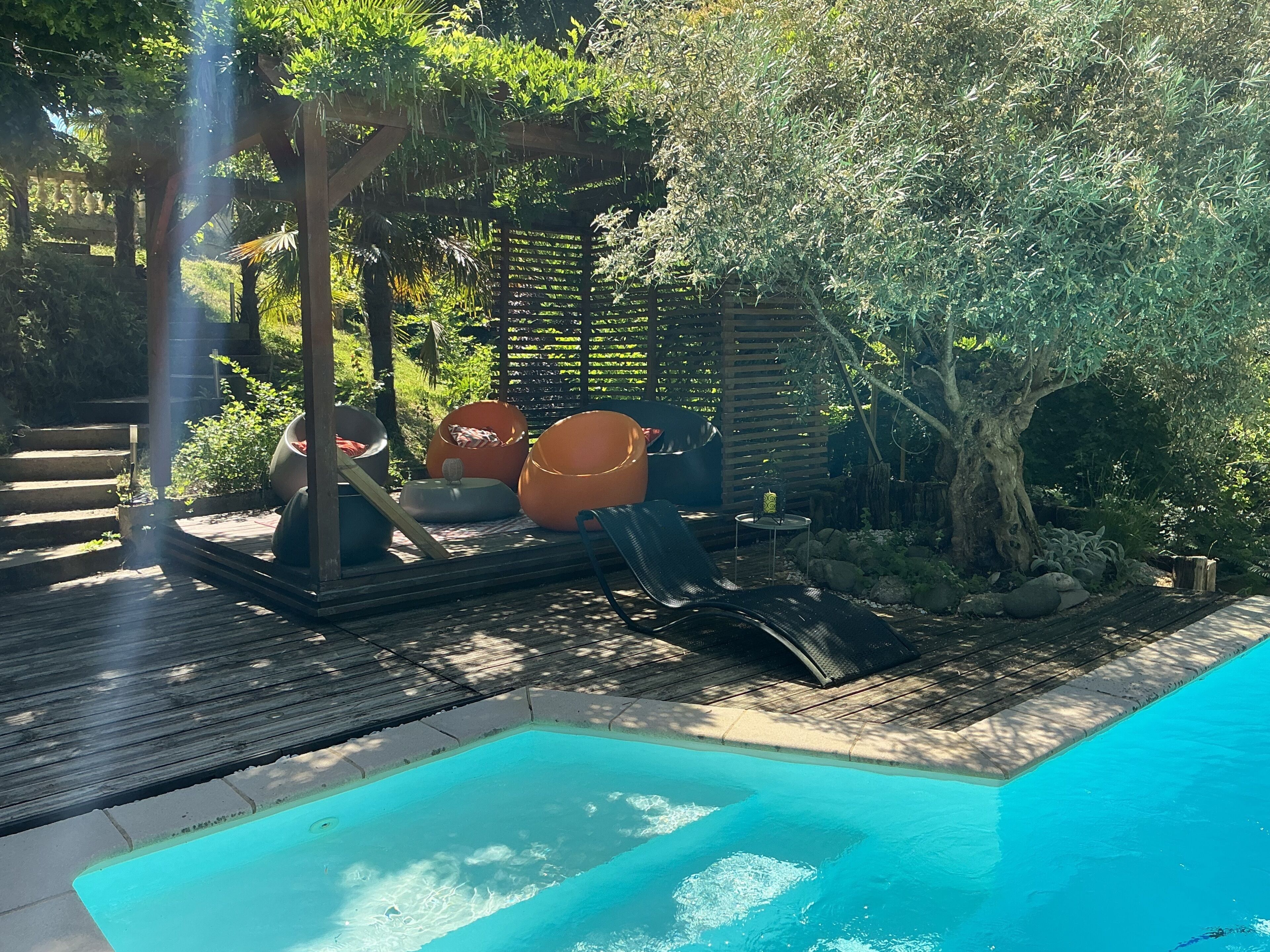 A poolside area with a wooden deck, a small pool, and outdoor seating including bean bags and a lounge chair.