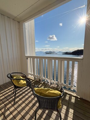 Ein Balkon mit zwei Korbstühlen, einem karierten Boden und Blick aufs Meer.