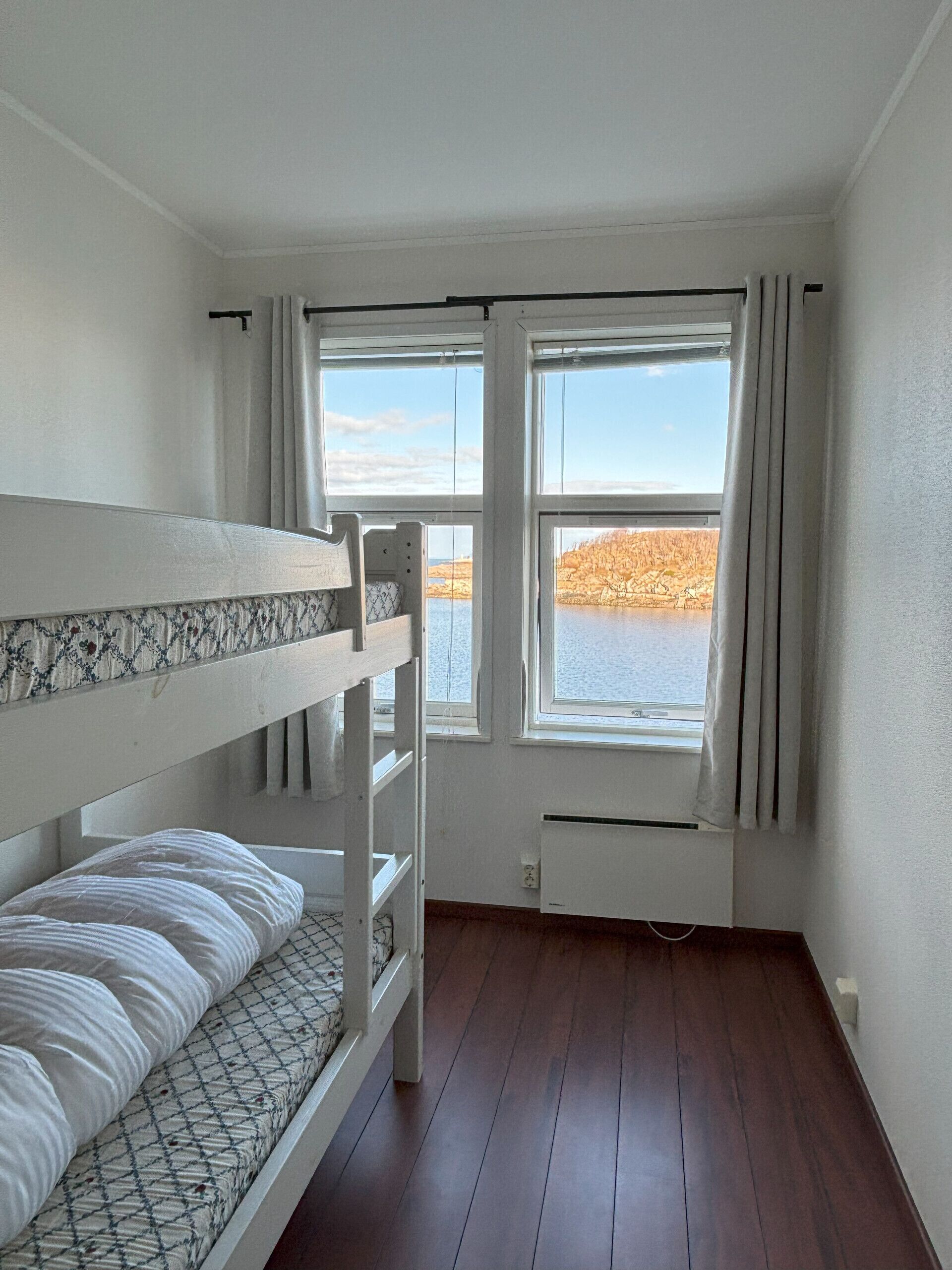Habitació amb literes, finestra amb cortines i vista a un llac.