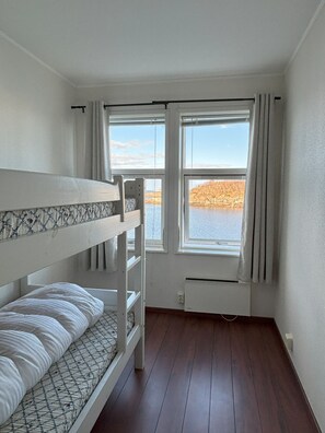 A room with bunk beds, a window with curtains, and a view of a lake. - Apartment by the sea in Henningsvær (Vågan)