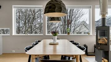 Een moderne eetruimte met een houten tafel, zwarte stoelen, een geometrische hanglamp en uitzicht op met sneeuw bedekte bomen door grote ramen.